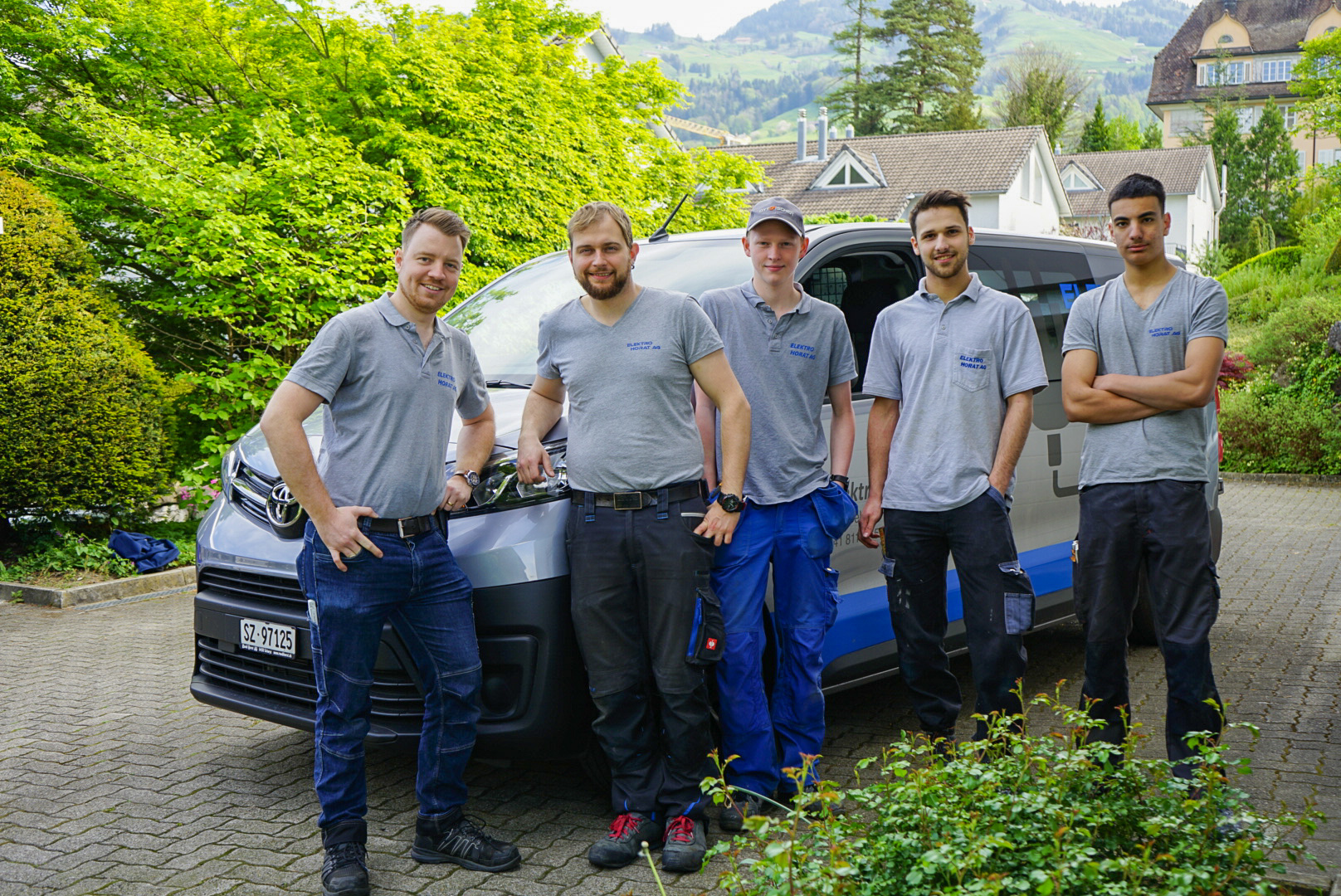 Fünf Mitarbeitende in grauen Firmenshirts vor dem Firmenwagen
