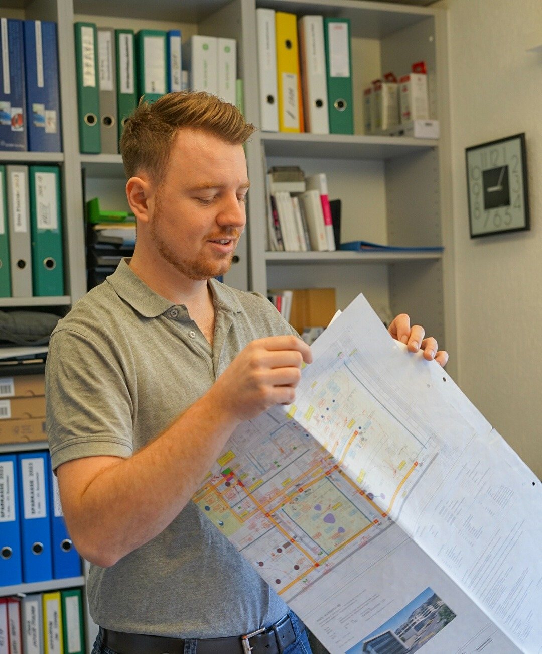 Mitarbeiter liest einen Bauplan vor einem Büroregal